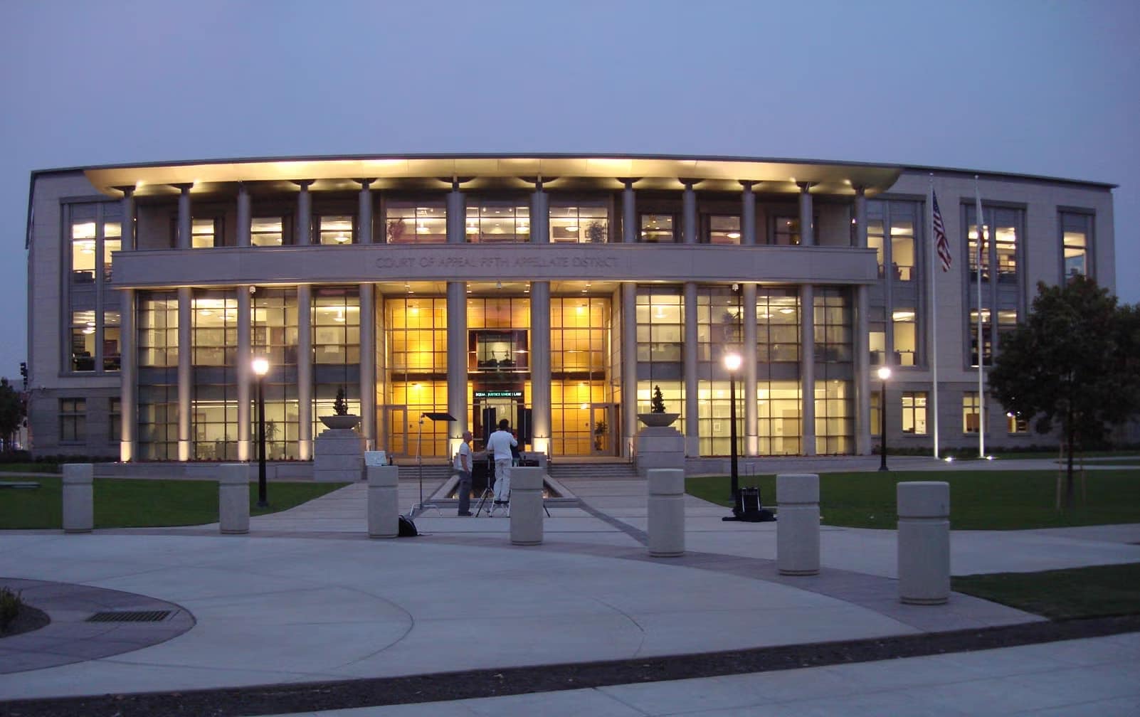 A modern courthouse building illuminated at dusk, showcasing large windows and a symmetrical façade. In the foreground, a few individuals walk along a pedestrian pathway. This image relates to the topic of California arbitration agreement unconscionability.
