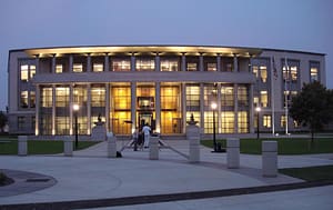 A modern courthouse building illuminated at dusk, showcasing large windows and a symmetrical façade. In the foreground, a few individuals walk along a pedestrian pathway. This image relates to the topic of California arbitration agreement unconscionability.