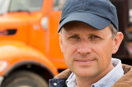 A man wearing a baseball cap and a brown jacket stands in front of an orange truck. He appears to be focused and calm, with a slightly serious expression. This image relates to themes of associational disability discrimination in California.