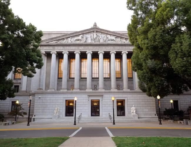 The California Court of Appeal building, featuring a neoclassical design with tall columns, statues on either side of the steps, and large windows illuminating the entrance. The scene includes lush greenery and street lamps in the foreground, relevant to the CSU anti-SLAPP retaliation case.